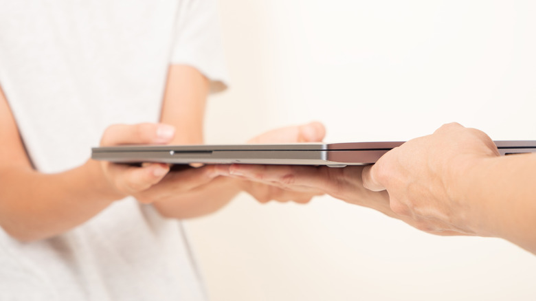 One person handing over a laptop to another person