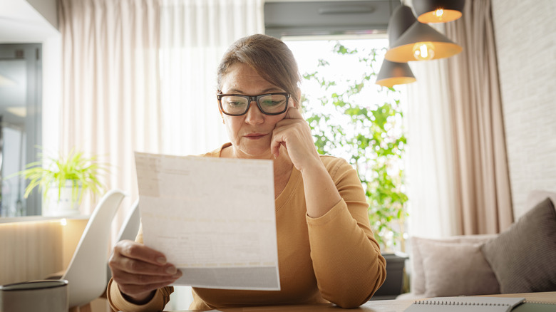 Woman with glasses in a living room examining a piece of paper