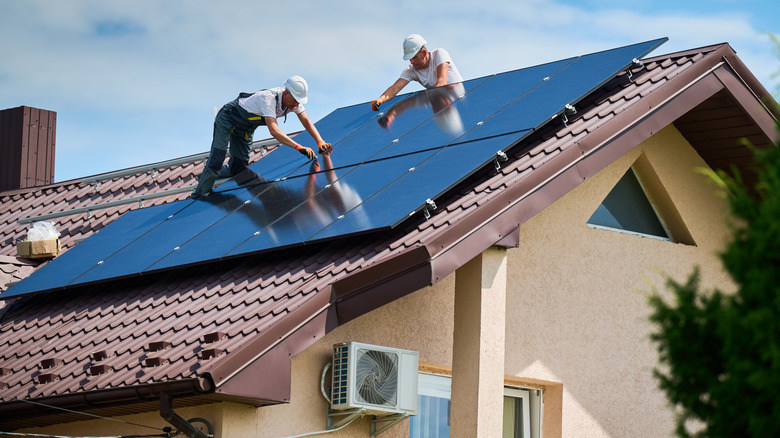 Two workers installing solar panels on a red clay roof
