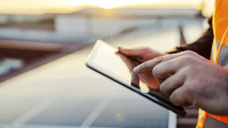 Close up sideview of hand holding a tablet with solar panels in the background