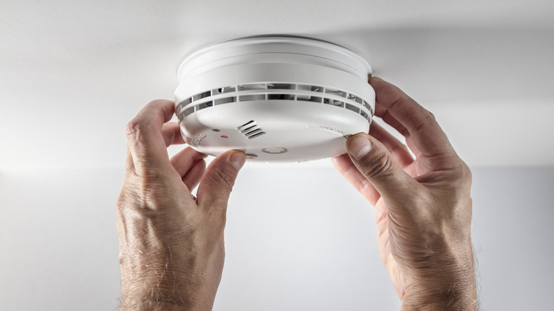 Two hands testing a smoke detector on the ceiling