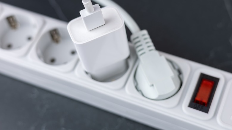 A surge protector power strip on the ground with a couple of occupied plugs