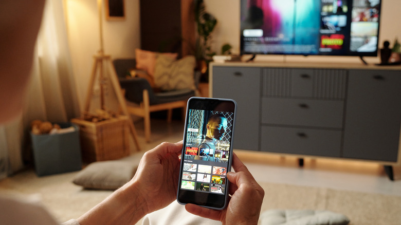 A smartphone casting to a television in the background