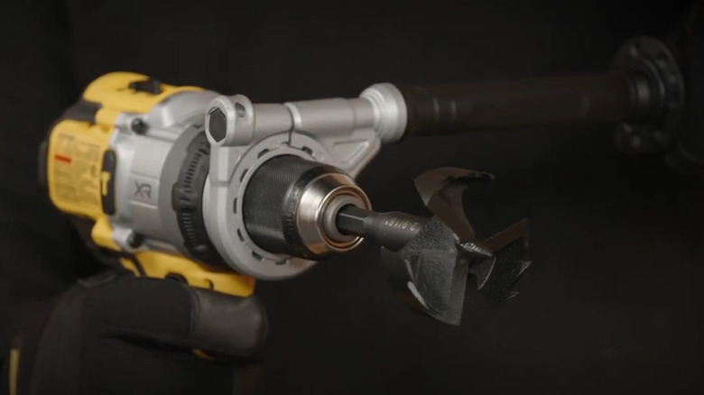 Person holding a hammer drill with a side handle and boring bit