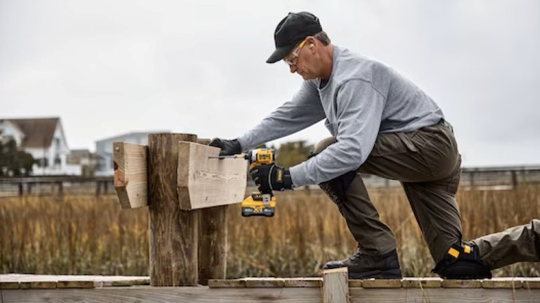 person installing a long fastener through three pieces of wood