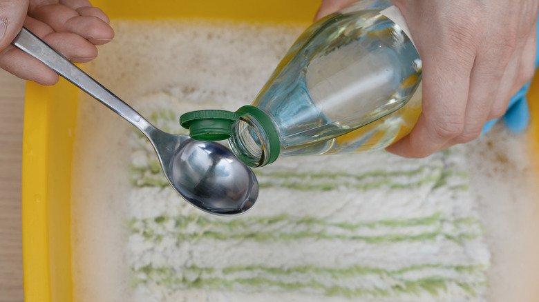Hand pouring clear liquid into a silver spoon