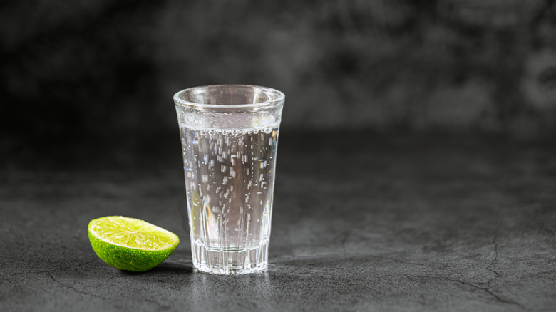 Clear glass of liquid with a lime against a black background