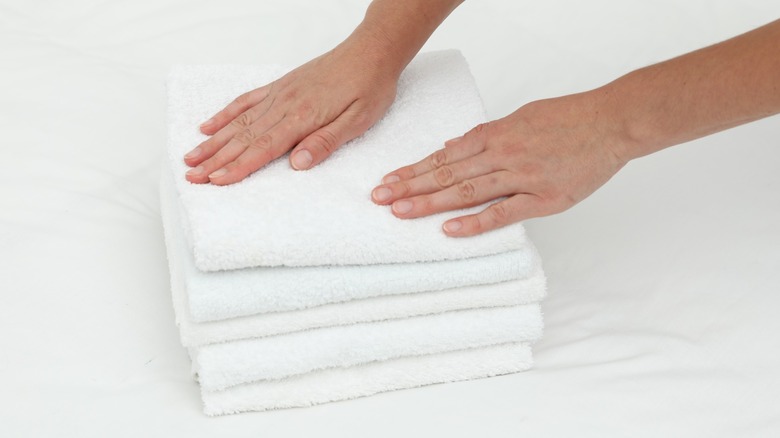 Hands pressing down on a stack of white terry cloth towels