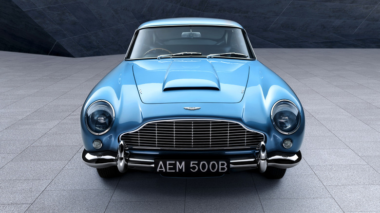 Blue Aston Martin DB5 sports car seen from directly in front against a modern architecture background