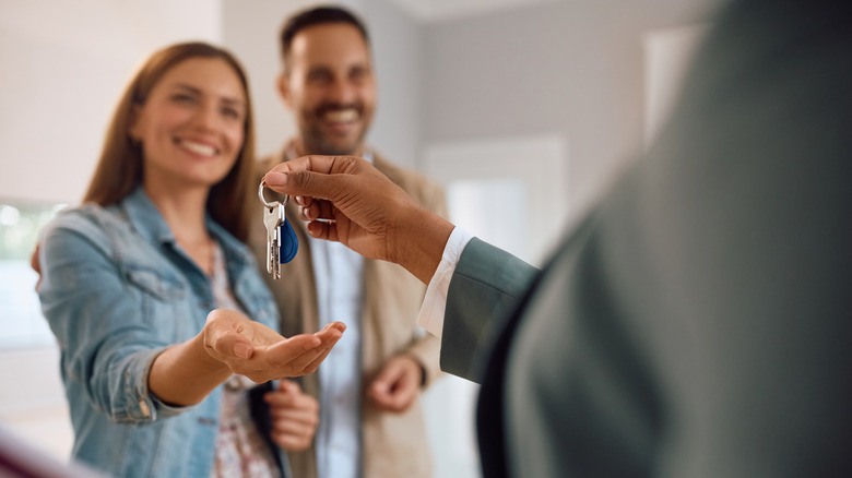 Couple smiling while receiving keys from a person in a suit