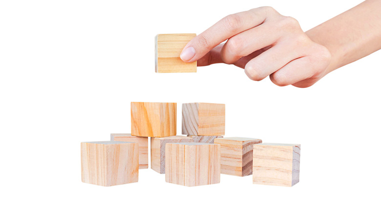 A hand adding a wooden building block to a structure