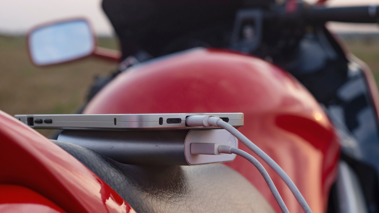 A smartphone being charged with a powerbank, both placed on top of a motorcycle