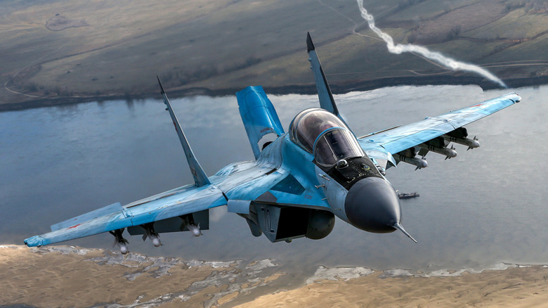 MiG-35 fighter jet seen in flight from in front with water and a shoreline below it
