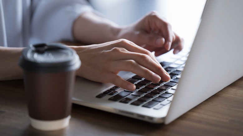 Hands typing on keyboard with coffee in foreground
