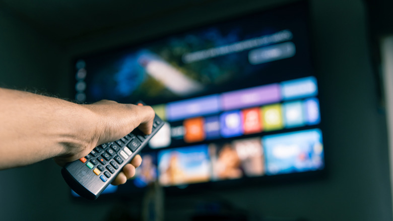 A hand holding a remote control browsing apps on a smart TV