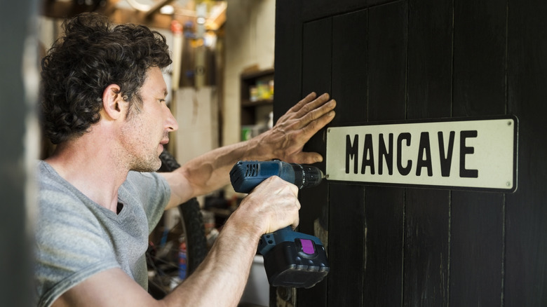 A person fixing a man cave sign to a door using a cordless drill