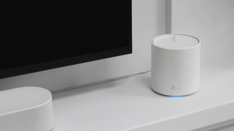 Mesh wi-fi system set up on white countertop beside TV