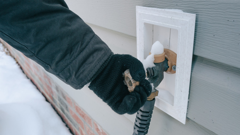 A gloved hand struggles with a frozen faucet