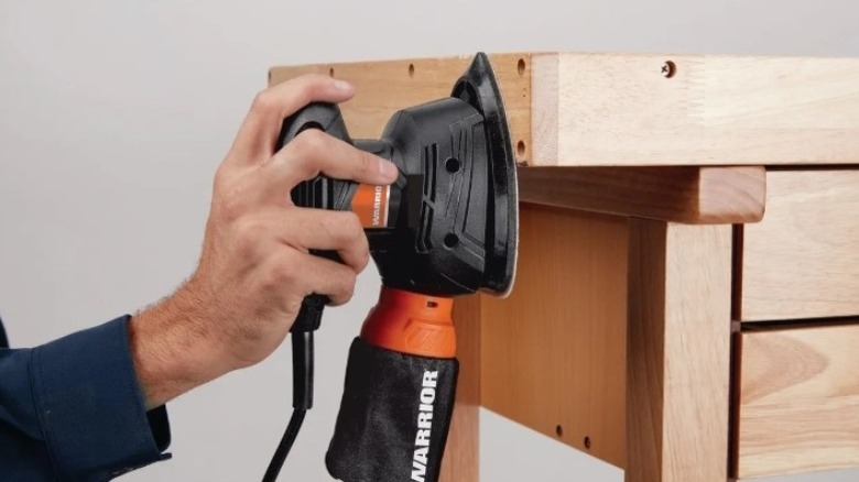 A hand using a Warrior corner sander on a wood table