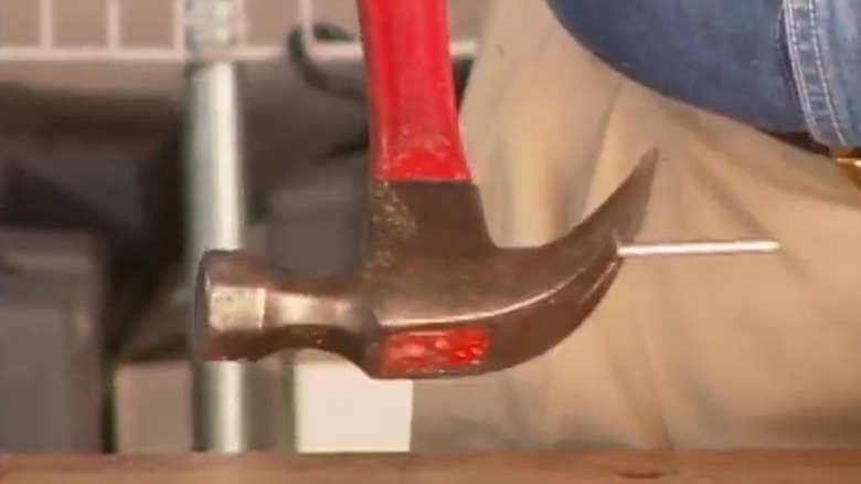 A nail propped between the claws of a hammer
