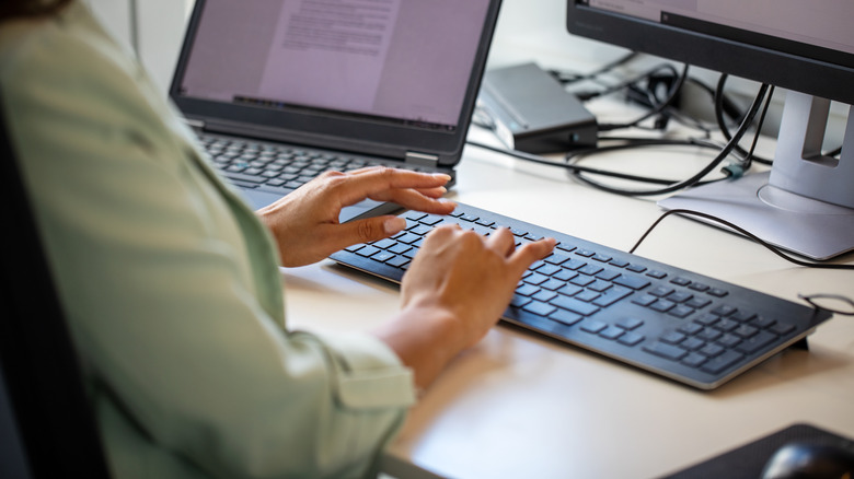 A woman working at a desk with multiple monitors and a keyboard
