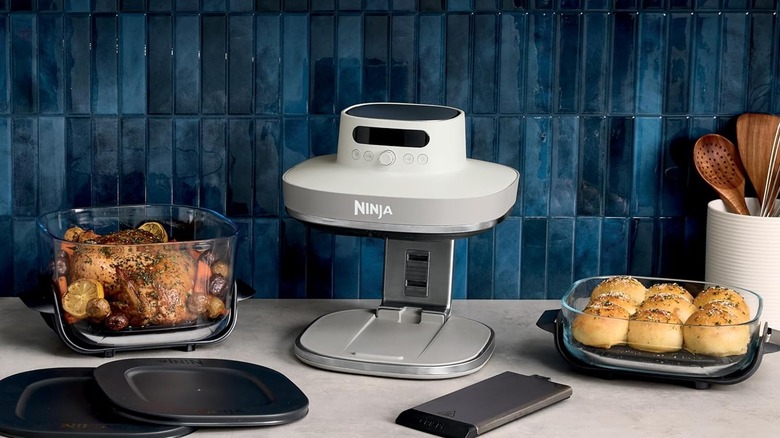 Ninja Crispi air fryer kept in a kitchen among some utensils carrying food
