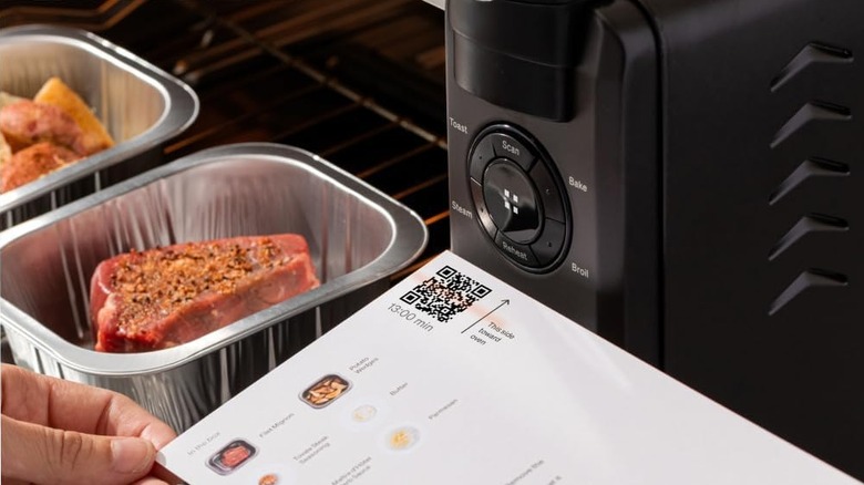 A person holding a manual with a QR code next to a mini oven