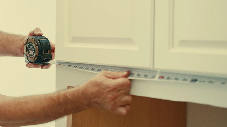 A person measuring kitchen cabinets with a tape measure