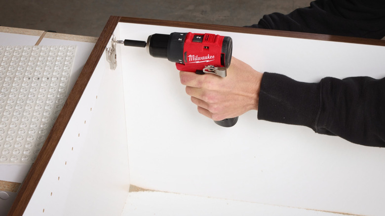 A person using a Milwaukee driver to build furniture.