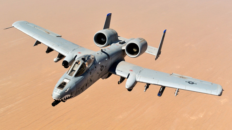 An A-10 Thunderbolt II flying with the desert ground underneath