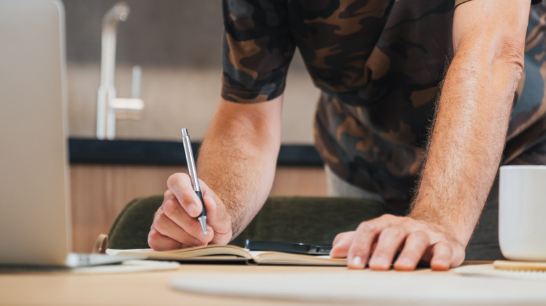 Man makes a list with a laptop in the foreground