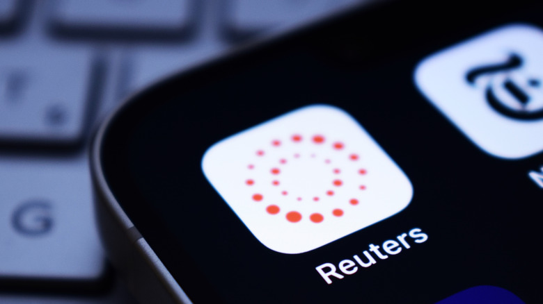 The Reuters app tile on a smartphone with a computer keyboard seen in the background.