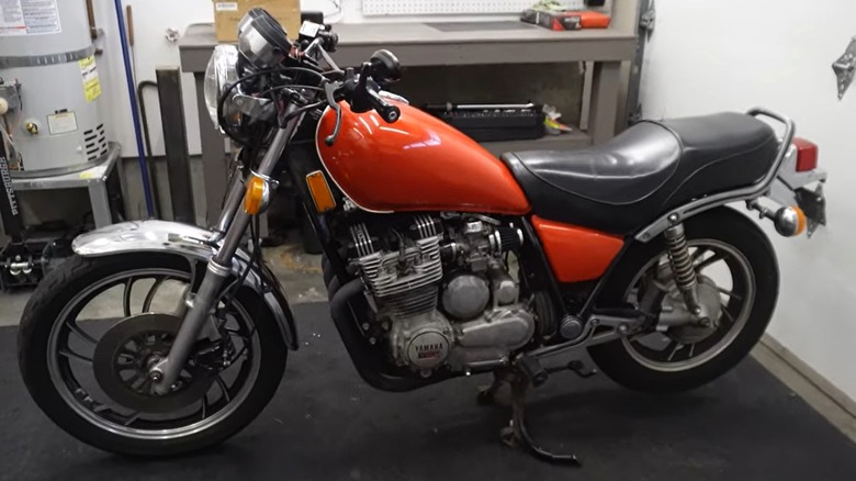 A well-kept orange-red Yamaha XJ650 stands inside a garage workspace, surrounded by tools and equipment.