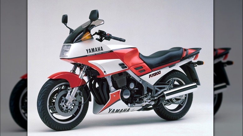 A 1985 red and white Yamaha FJ1200 sport-tourer is displayed in a studio setting, emphasizing its aerodynamic fairing and bold '80s styling.