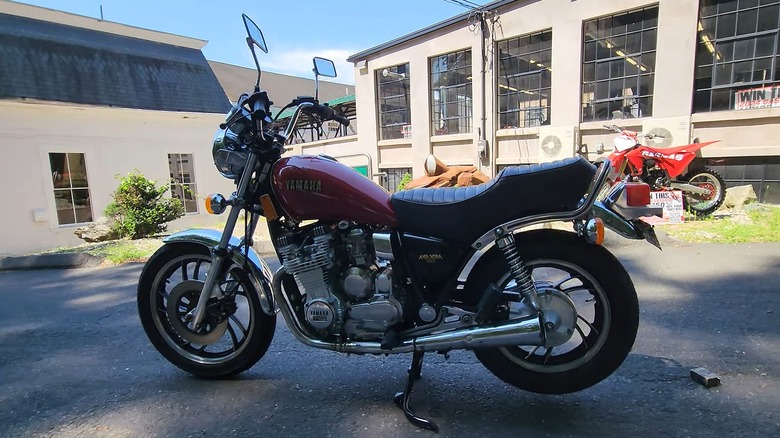 A vintage red Yamaha XJ650 rests outside a motorcycle shop under bright daylight, highlighting its chrome details and classic lines.