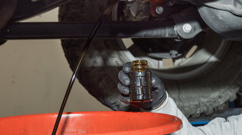 A scientist taking a sample of motor oil as its being drained
