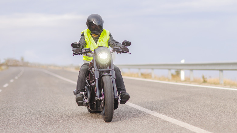 A person  with a reflective vest riding a cruiser in a highway