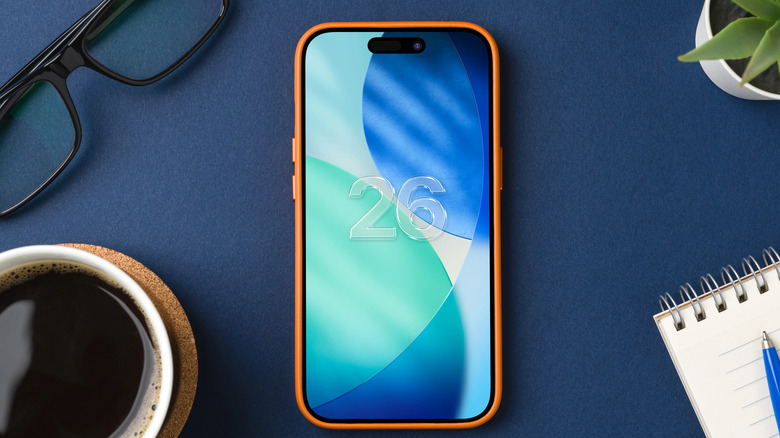 iPhone on a blue desk with iOS 26 splash screen on