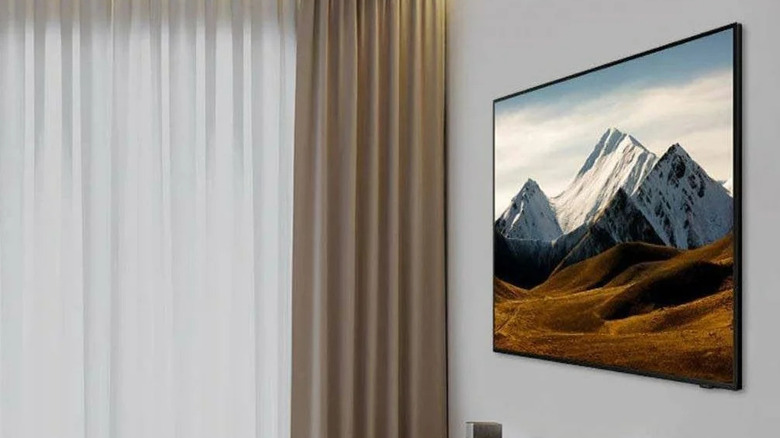 A Samsung 55-inch 4K Crystal UHD Smart TV hanging on a wall next to some curtains with mountains on the display.