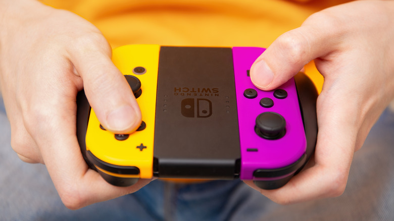 A pair of Joy-Cons being held by a person in a plastic controller grip