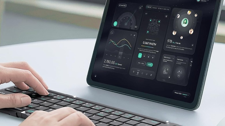 A person typing on a keyboard while working on an iPad
