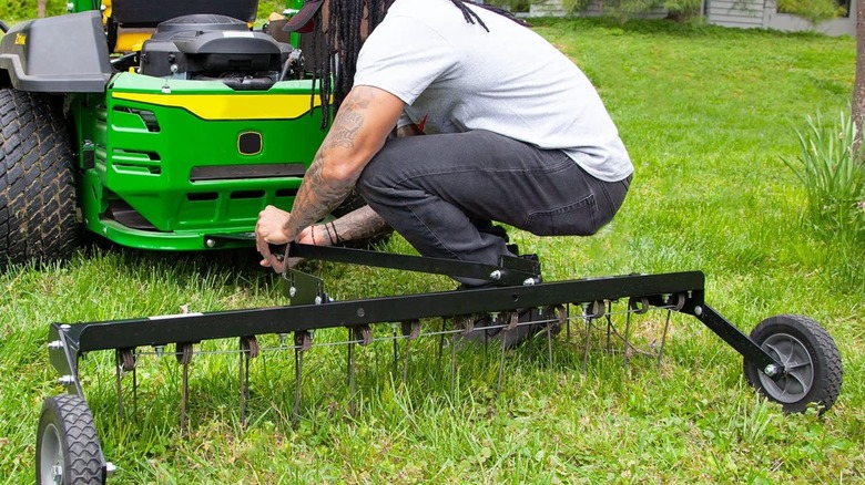 A person attaches a dethatcher to a riding mower.