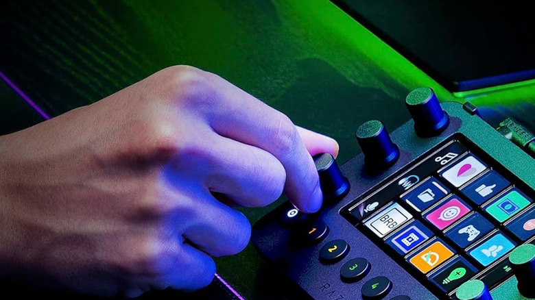 Razer Stream Controller with icons lit up, while a hand turns a knob on the controller