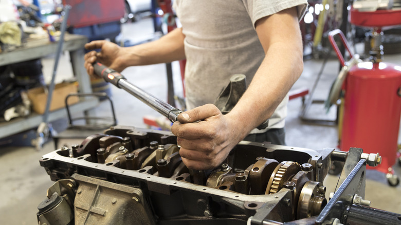 A close-up of a mechanic working on an engine inside a shop.