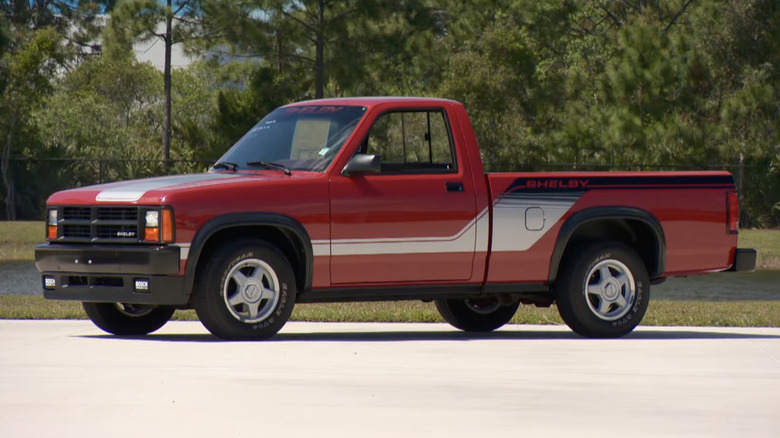 A red 1989 Shelby Dakota performance truck parked outside with grass and trees in the background.