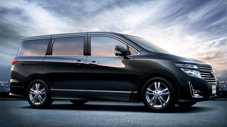 Black Nissan Elgrand parked with city lights in the distance