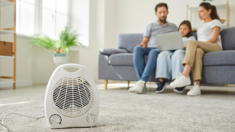A small electric heater on the floor near people on a couch.