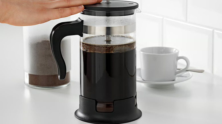 French press separate coffee grinds with a hand holding the top in place