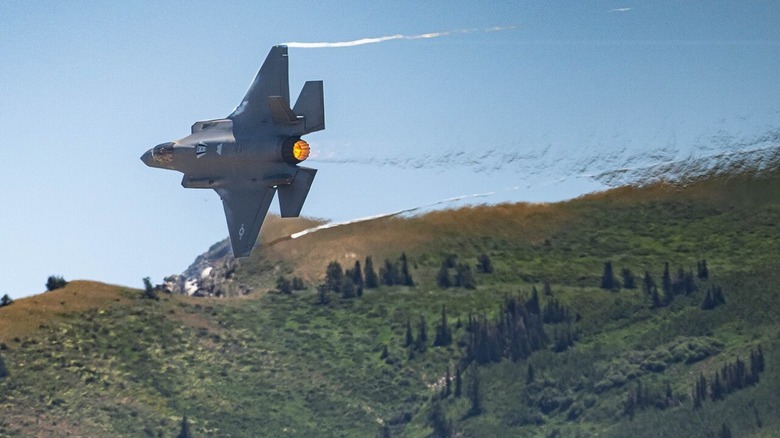 F-35A Lightning II flying over grassy terrain.