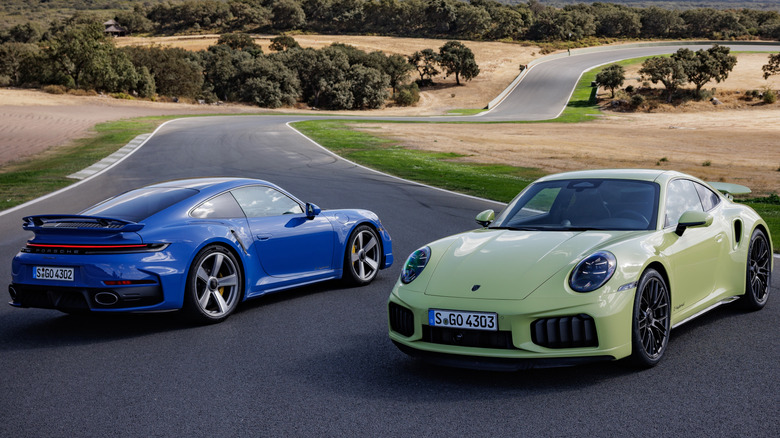 A blue and green 2026 Porsche 911 Turbo S sports cars parked on a race track.